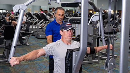 私人教练帮助男人上身锻炼设备。